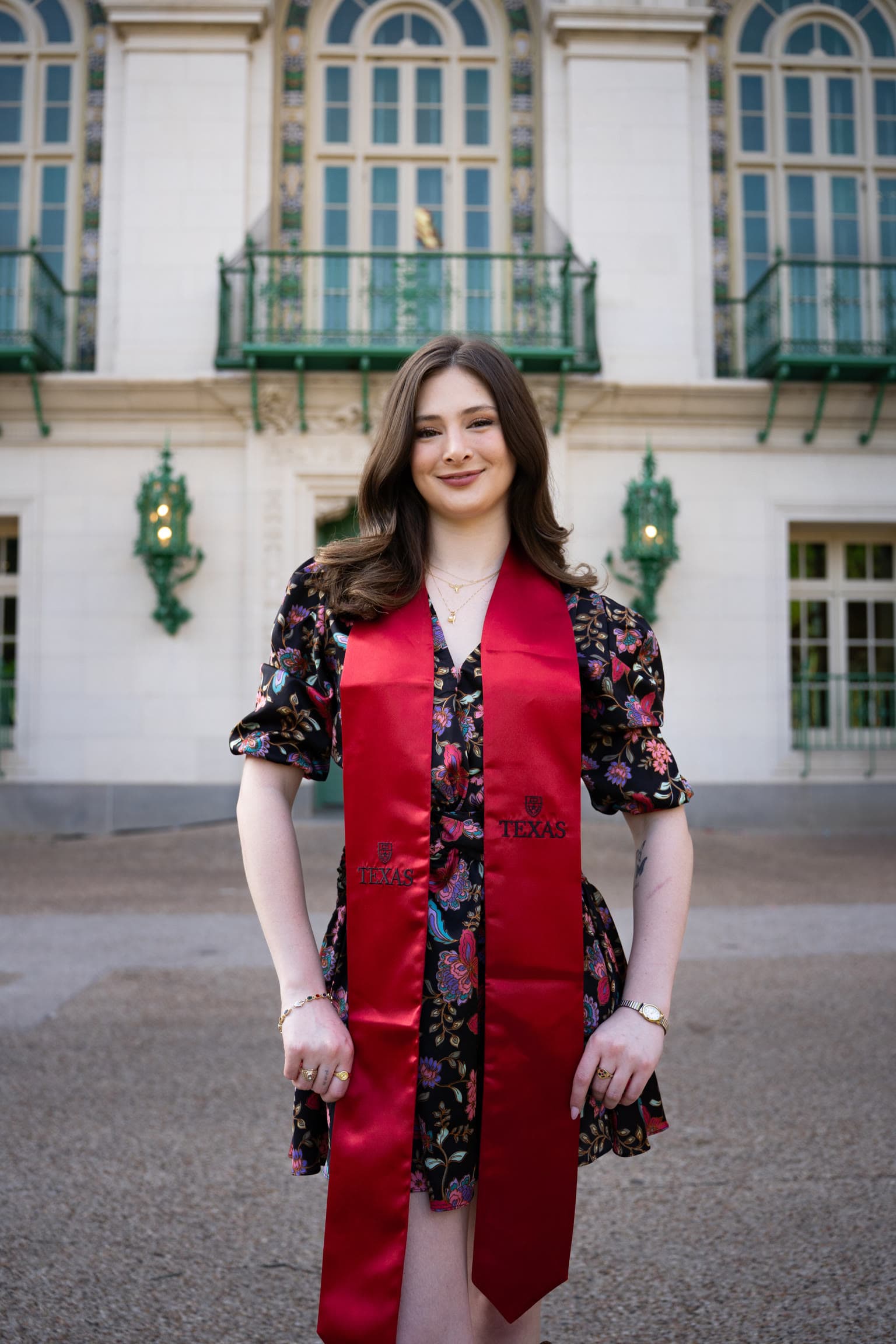 UT Austin graduate in a red stole outside the Littlefield Home